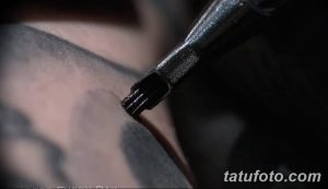 Фотография крупным планом тату-аппарата во время работы. Видна игла, проникающая в кожу, и детали аппарата.